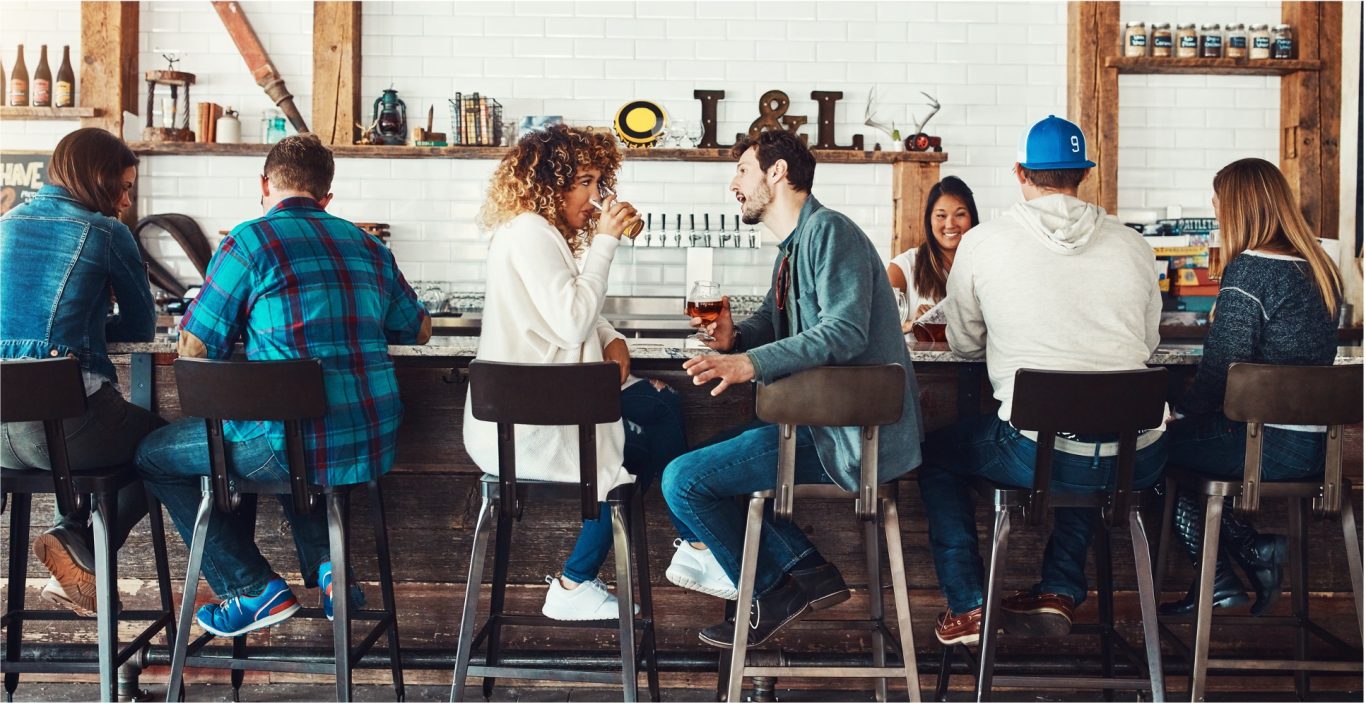 Kommunikation an der Bar Eine Gruppe von Menschen sitzt an einer Bar und genießt Getränke und Gespräche.