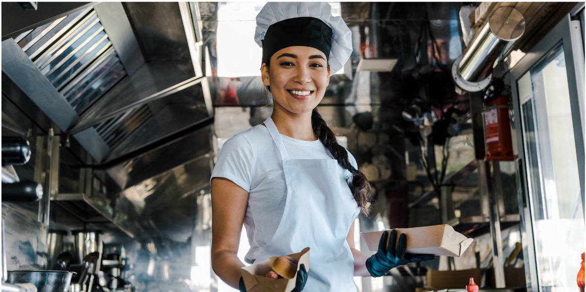 Asia Foodtruck Lächelnde Köchin in einem Foodtruck mit Kochutensilien in der Hand.